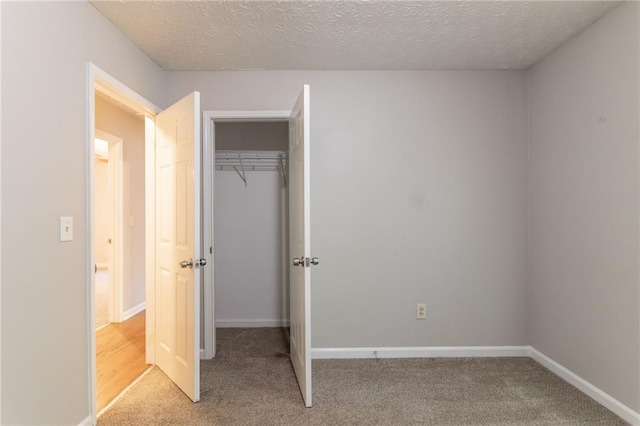 unfurnished bedroom featuring a closet, a textured ceiling, baseboards, and light carpet