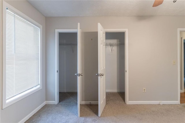 unfurnished bedroom with multiple closets, baseboards, a ceiling fan, and light colored carpet