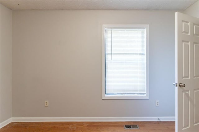 spare room featuring visible vents, baseboards, and wood finished floors