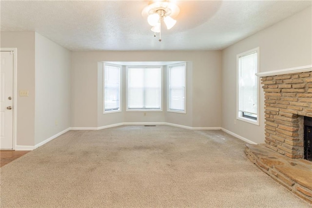 unfurnished living room with carpet floors, baseboards, a ceiling fan, and a stone fireplace