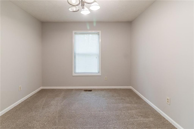 carpeted empty room featuring baseboards, visible vents, and a notable chandelier