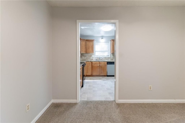 empty room with baseboards, a sink, and light carpet