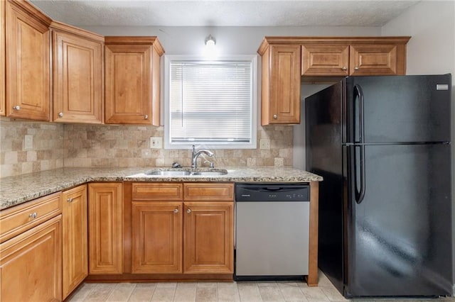 kitchen with light stone counters, a sink, freestanding refrigerator, backsplash, and stainless steel dishwasher