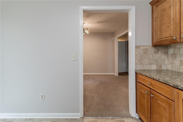 kitchen featuring baseboards, light colored carpet, a textured ceiling, brown cabinets, and tasteful backsplash