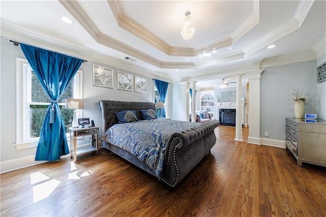 bedroom featuring decorative columns, wood-type flooring, crown molding, and a raised ceiling