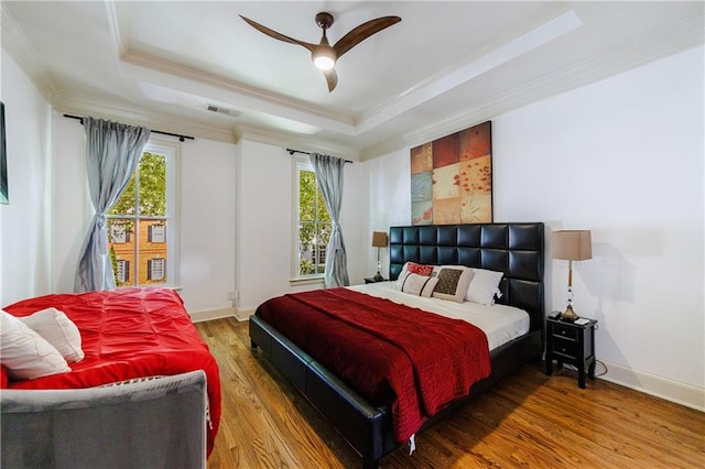 bedroom with ceiling fan, wood-type flooring, ornamental molding, and a tray ceiling