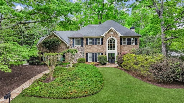 colonial-style house featuring french doors, a chimney, brick siding, a front yard, and view of scattered trees