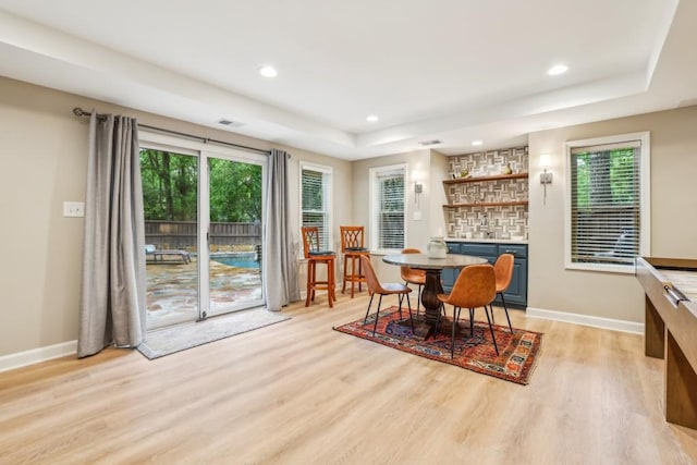 dining space featuring light wood-style floors, bar with sink, a raised ceiling, recessed lighting, and baseboards