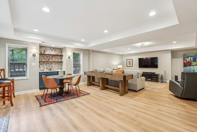 dining room featuring a tray ceiling, bar, light wood-style floors, recessed lighting, and baseboards