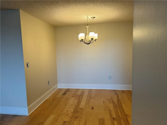 unfurnished dining area featuring a textured ceiling, baseboards, a notable chandelier, and light wood-type flooring