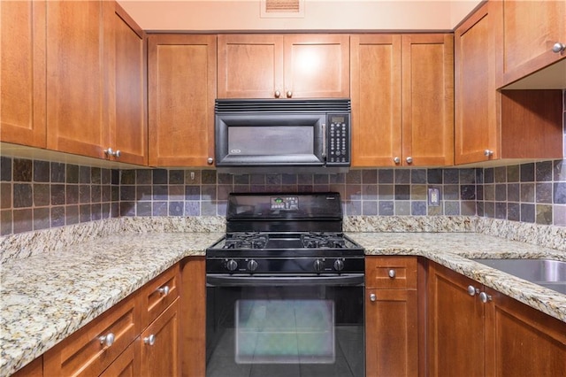 kitchen with decorative backsplash, brown cabinetry, black appliances, and light stone countertops