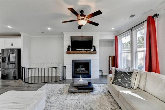 living room featuring ornamental molding, wood-type flooring, a large fireplace, and ceiling fan