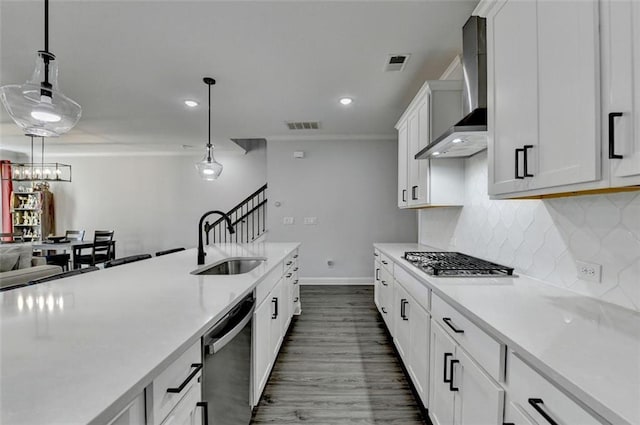 kitchen with sink, wall chimney range hood, appliances with stainless steel finishes, white cabinetry, and hanging light fixtures