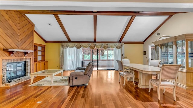 living room with vaulted ceiling with beams, a fireplace, wood walls, and light hardwood / wood-style flooring