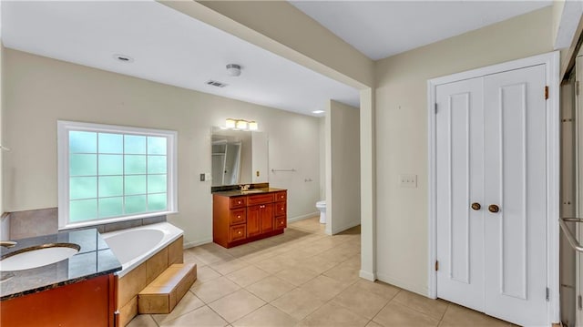 bathroom featuring vanity, toilet, tile patterned floors, and a relaxing tiled tub