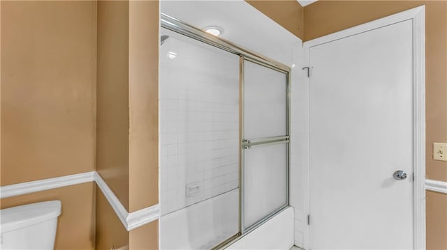 bathroom with combined bath / shower with glass door and toilet