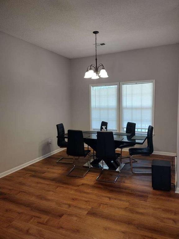 dining room featuring a chandelier, visible vents, a textured ceiling, and wood finished floors