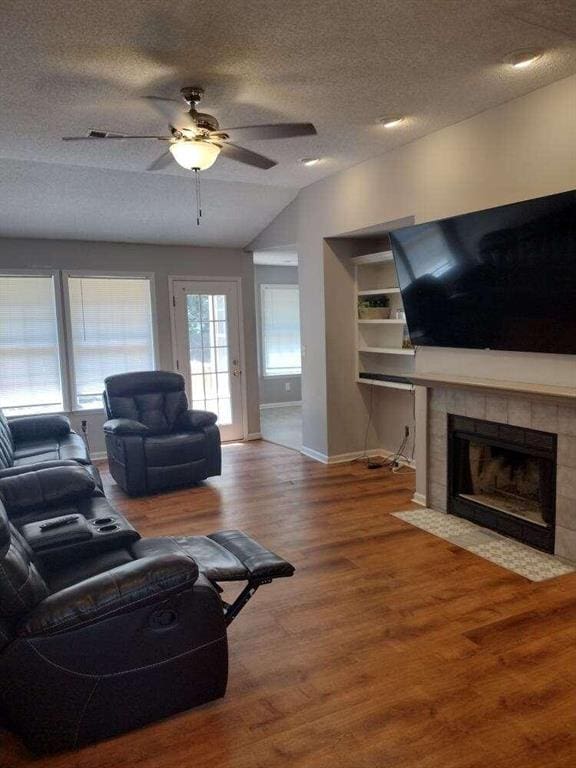 living room with baseboards, a ceiling fan, a textured ceiling, wood finished floors, and vaulted ceiling