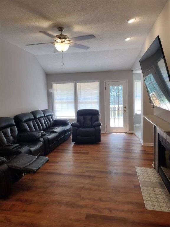 living area featuring ceiling fan, vaulted ceiling, wood finished floors, and a textured ceiling