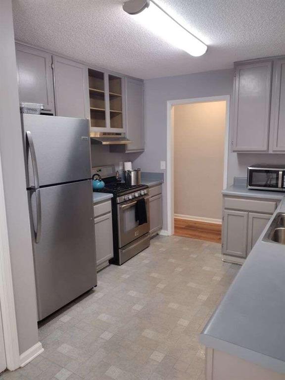 kitchen featuring gray cabinets, under cabinet range hood, baseboards, and stainless steel appliances