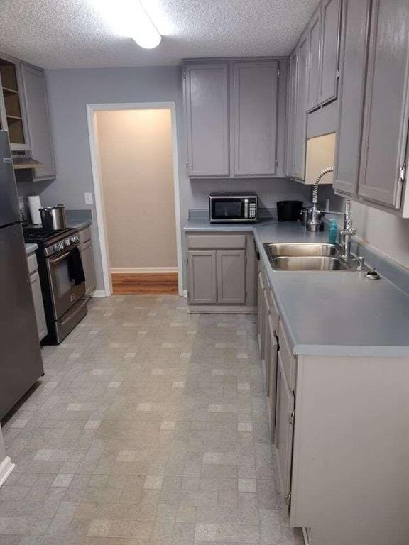 kitchen featuring gray cabinets, a textured ceiling, a sink, and appliances with stainless steel finishes