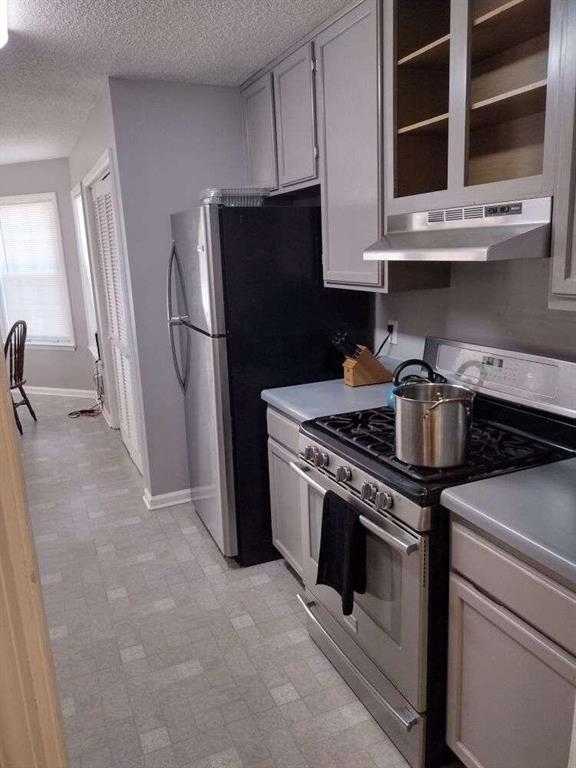kitchen with stainless steel range with gas cooktop, light floors, a textured ceiling, under cabinet range hood, and light countertops