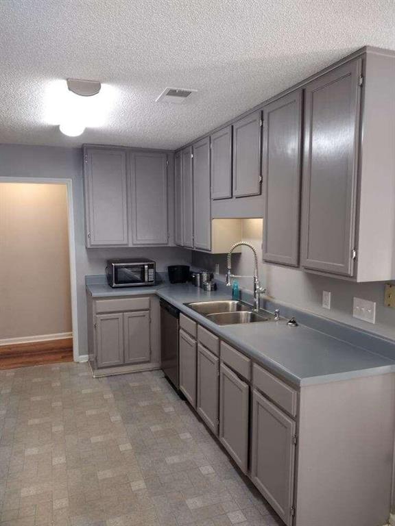 kitchen with a textured ceiling, gray cabinets, dishwasher, a sink, and baseboards