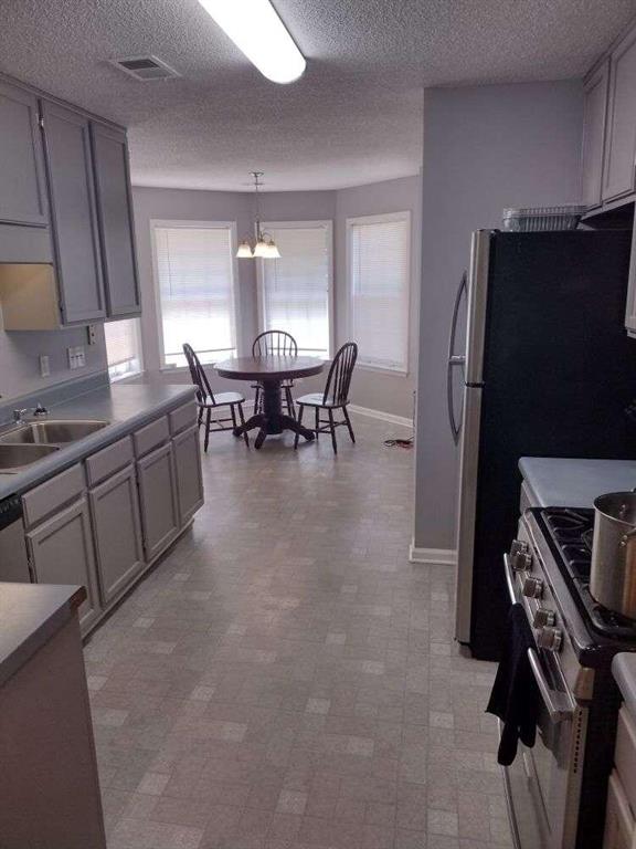 kitchen with a textured ceiling, a chandelier, a sink, stainless steel appliances, and decorative light fixtures