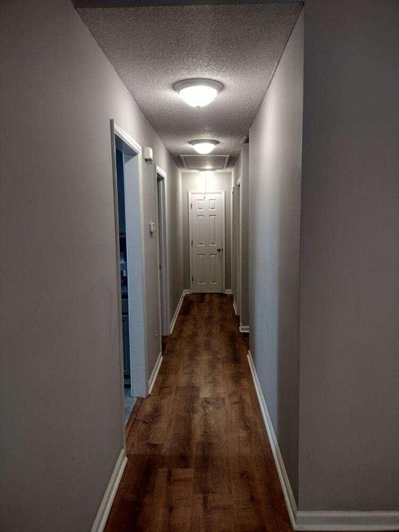 hall featuring baseboards, a textured ceiling, and dark wood finished floors