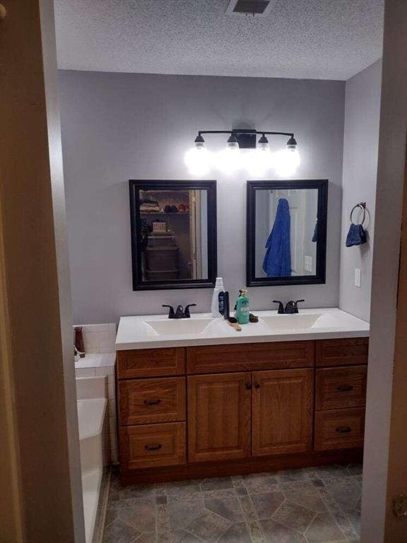 full bathroom featuring double vanity, a bath, a textured ceiling, and a sink