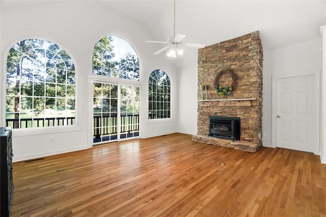 unfurnished living room with hardwood / wood-style floors, high vaulted ceiling, a stone fireplace, and ceiling fan