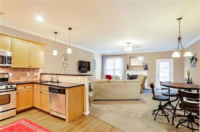 kitchen with sink, kitchen peninsula, decorative light fixtures, appliances with stainless steel finishes, and light wood-type flooring