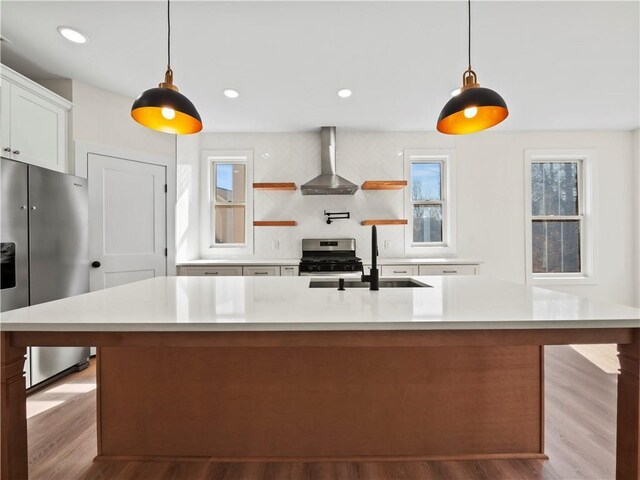 kitchen featuring wall chimney exhaust hood, stainless steel gas range, sink, decorative light fixtures, and white cabinets