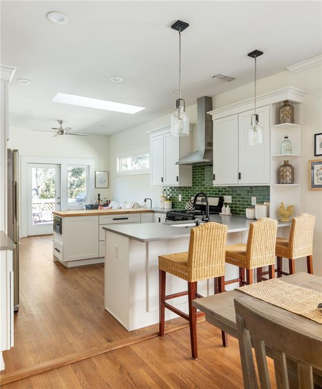 kitchen featuring light wood finished floors, wall chimney exhaust hood, freestanding refrigerator, a peninsula, and gas range oven