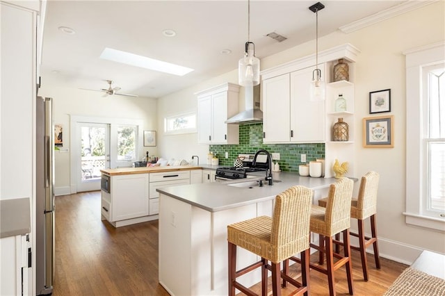 kitchen featuring a peninsula, dark wood-style flooring, a skylight, tasteful backsplash, and gas range oven