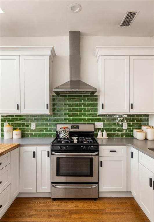 kitchen featuring visible vents, white cabinets, wall chimney range hood, stainless steel gas range, and light wood-type flooring