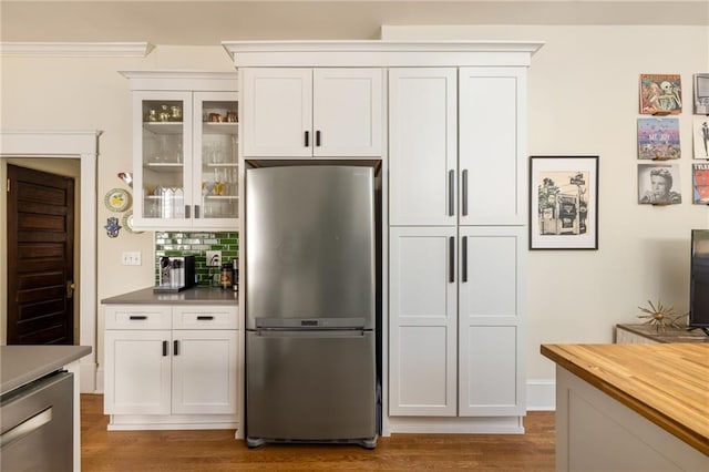 kitchen featuring backsplash, glass insert cabinets, freestanding refrigerator, white cabinetry, and wood finished floors