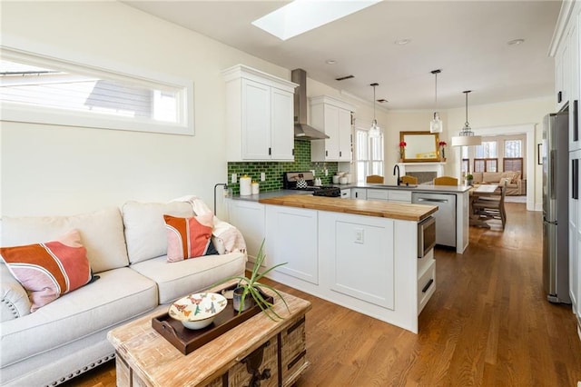 kitchen featuring wall chimney exhaust hood, butcher block counters, open floor plan, a peninsula, and stainless steel appliances