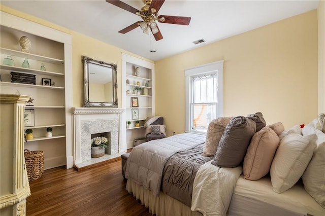 bedroom with a fireplace, wood finished floors, visible vents, and a ceiling fan