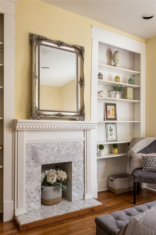 sitting room featuring built in features, a premium fireplace, and wood finished floors