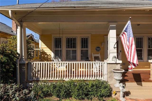 doorway to property featuring a porch and a shingled roof