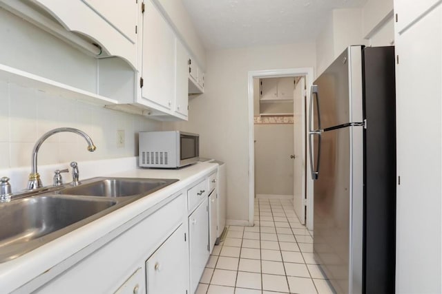 kitchen with a sink, light tile patterned flooring, freestanding refrigerator, white cabinetry, and light countertops