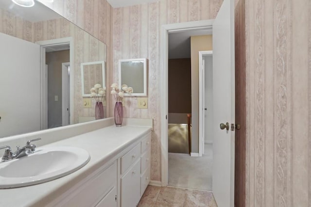 bathroom with baseboards, vanity, and wallpapered walls