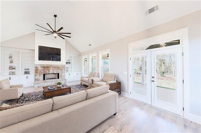 living room featuring french doors, light wood finished floors, a fireplace with raised hearth, visible vents, and ceiling fan