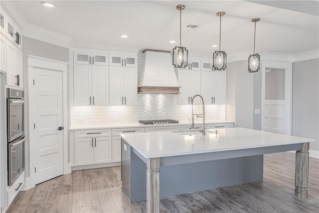 kitchen featuring white cabinetry, sink, pendant lighting, a center island with sink, and custom range hood