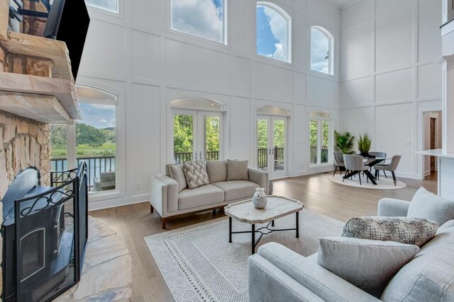 living room featuring a high ceiling, a stone fireplace, light hardwood / wood-style floors, and french doors