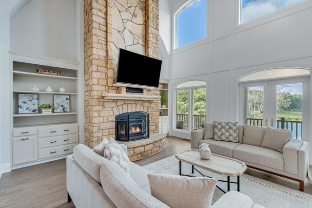 living room with a towering ceiling, a wealth of natural light, light wood-type flooring, and a stone fireplace