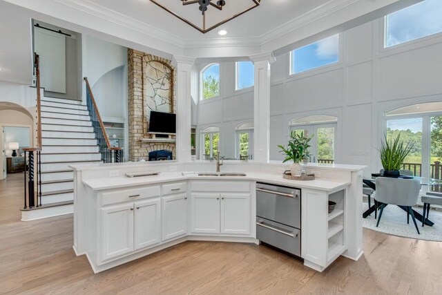 kitchen featuring light hardwood / wood-style flooring, white cabinetry, sink, a towering ceiling, and ornamental molding