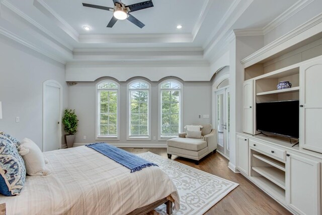 bedroom featuring a tray ceiling, ceiling fan, ornamental molding, and light hardwood / wood-style flooring