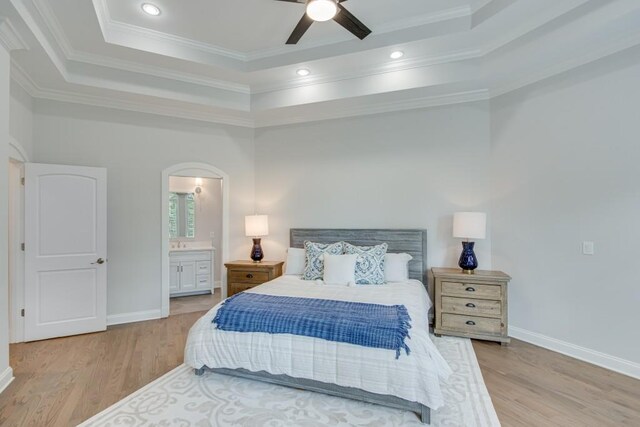 bedroom with ensuite bath, light hardwood / wood-style flooring, a raised ceiling, ceiling fan, and ornamental molding